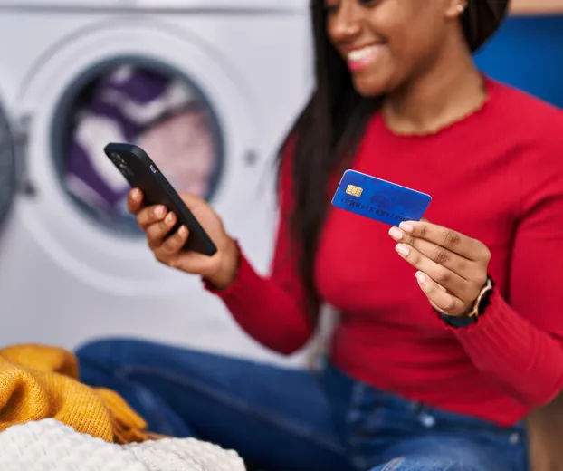 Woman Smiling And Holding Credit Card While Making Online Purchase With Smartphone